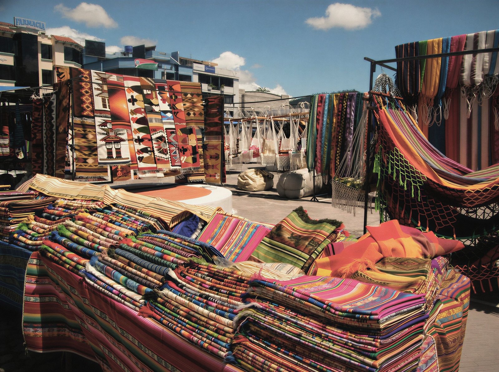 Woven textiles and blankets spread and hung for display in an open-air market square.